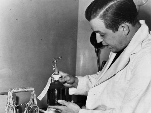 Black and white photo of Dr. Paul Hoxworth holding a glass bottle of donated blood. 