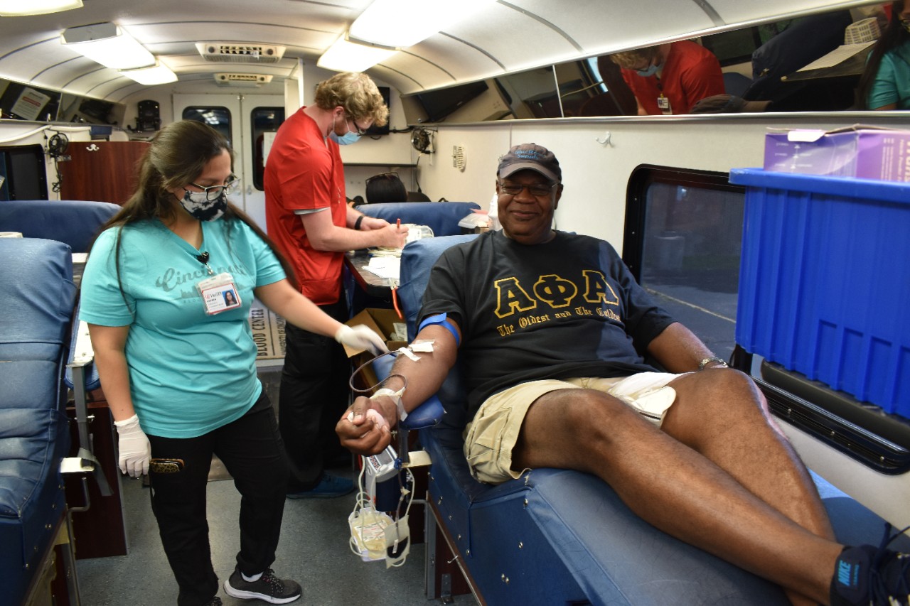 Myron Hughes in a donor chair on a Hoxworth bus, donating a unit of whole blood while a Hoxworth employee stands by