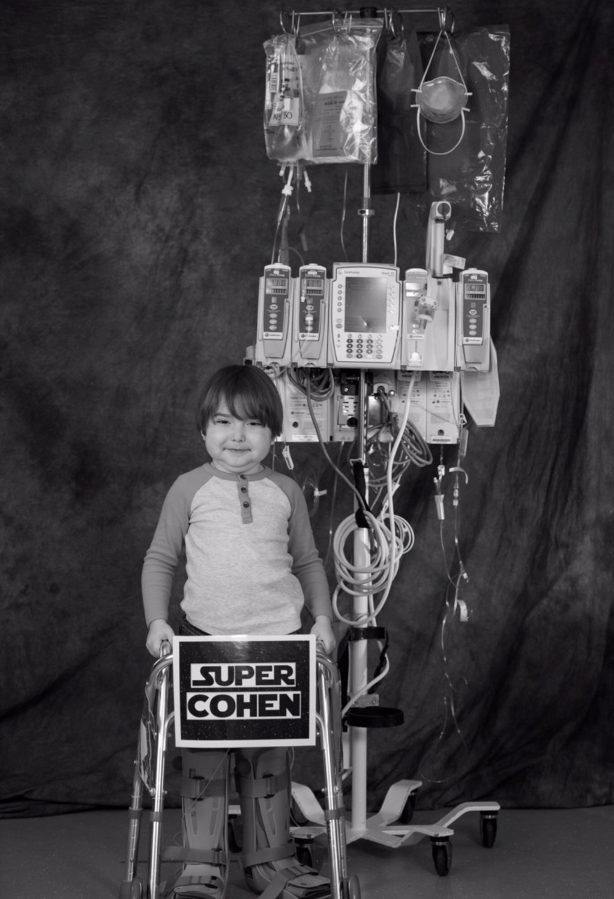 black and white photo of young Cohen standing in front of an IV pole with bags of nutrition and medicine
