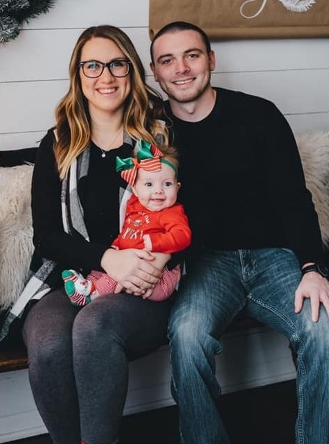 Kendra Stanley and her husband sitting with baby Addison in a Christmas outfit